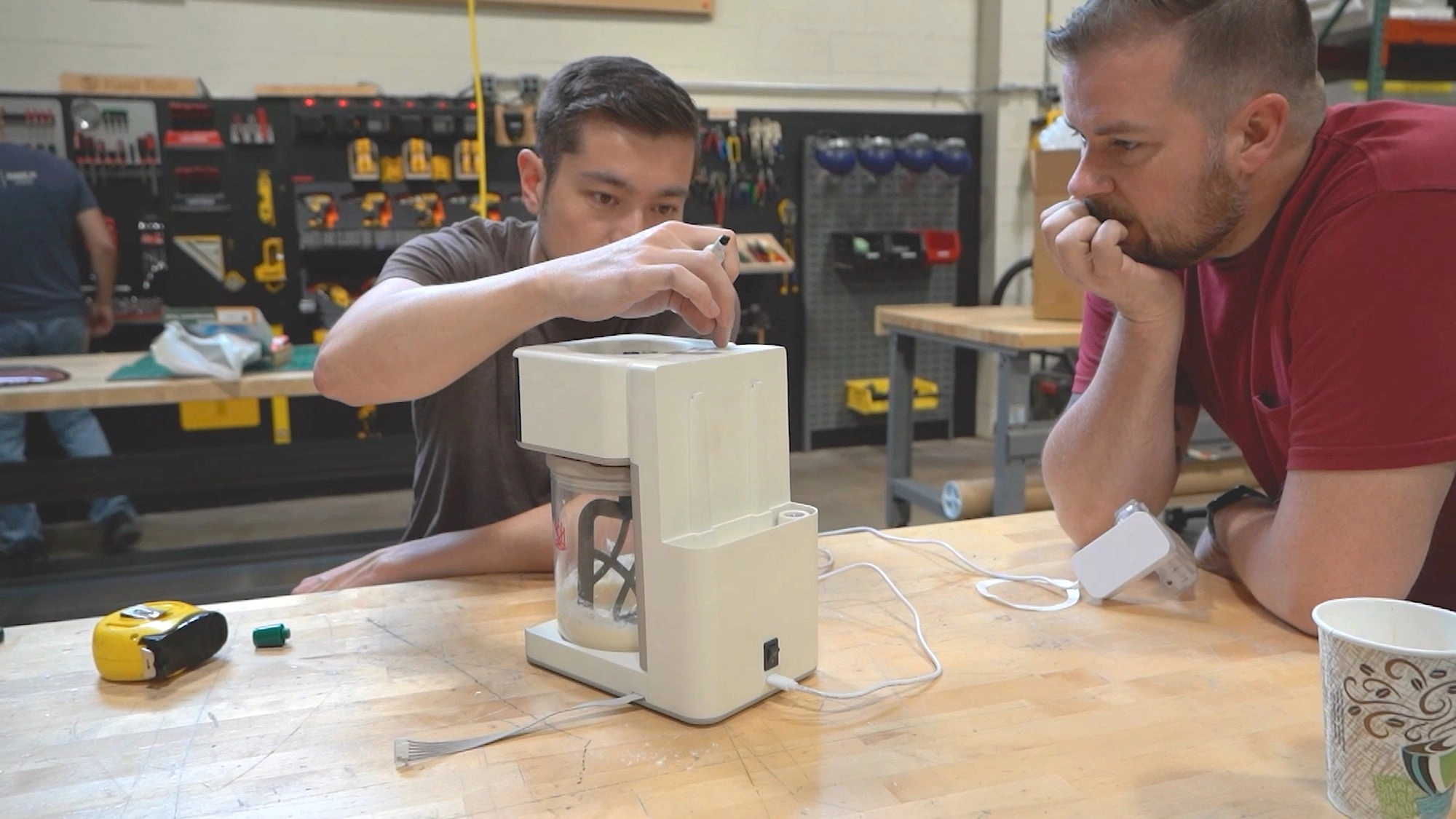 Two people at a workbench studying an early Sourdough Sidekick prototype