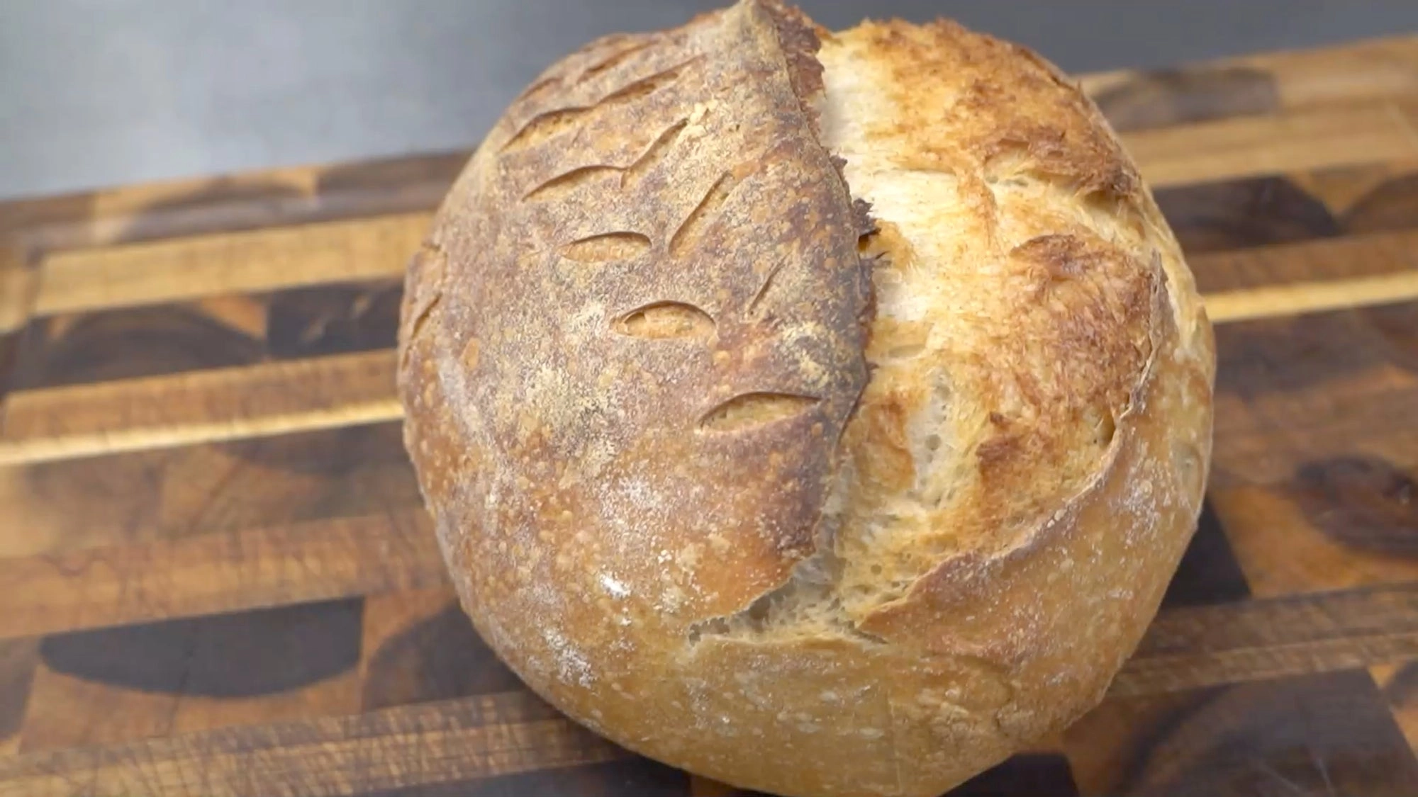 A scored sourdough loaf on a wooden board